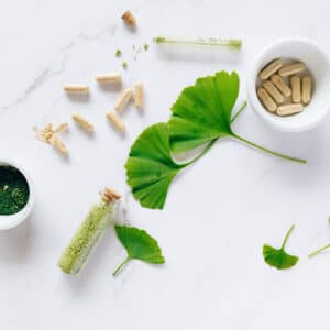 Herbal supplements are aesthetically spread on a marble countertop next to Gingko leaves and crushed up herbs | Nutritionist for Athletes and Weight Management in Idaho