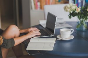 woman typing with planner and coffee cup